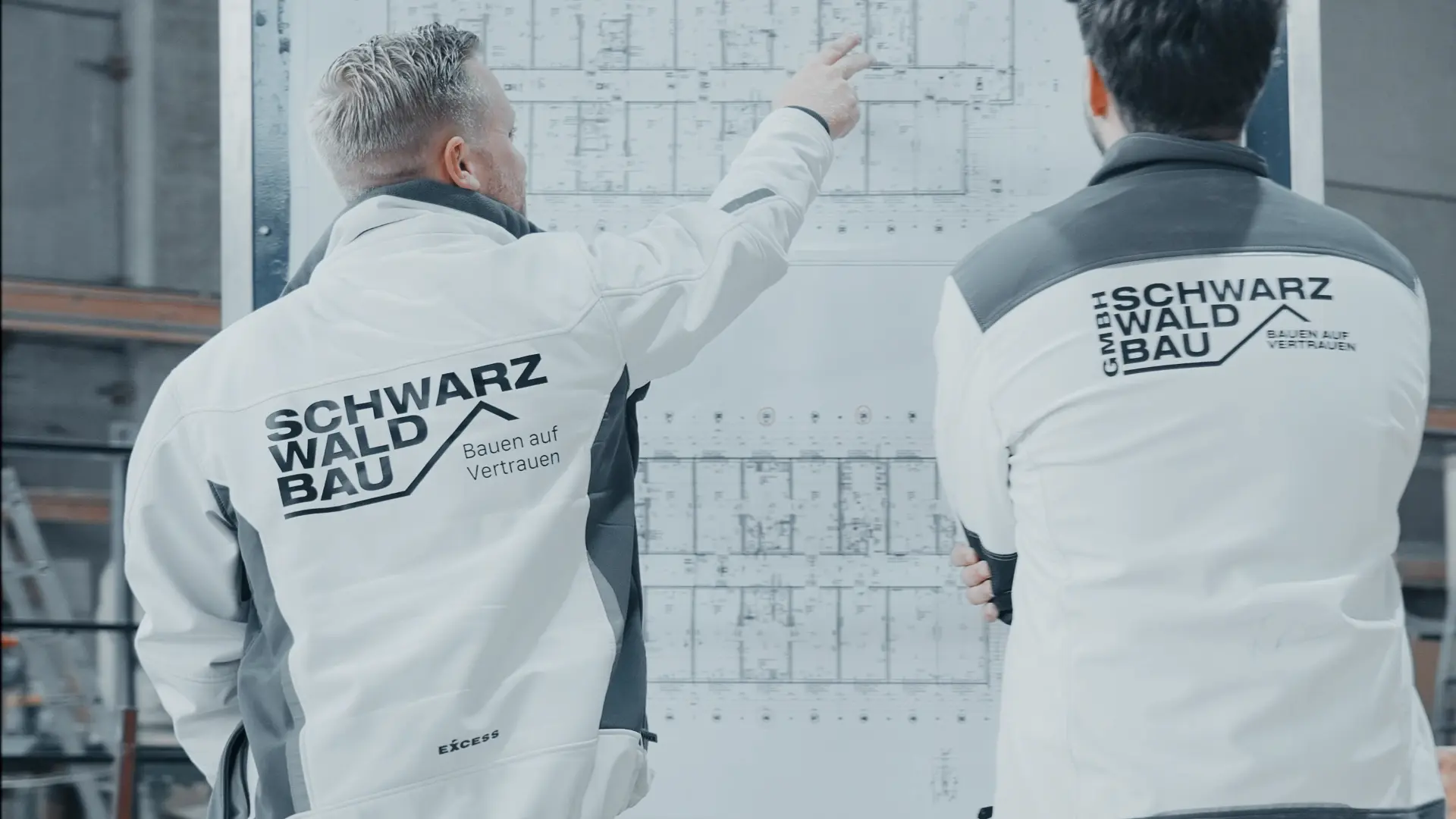 Zwei Mitarbeiter der Schwarzwaldbau GmbH besprechen einen Bauplan in der Werkhalle – Planung und Projektleitung im Schwarzwald